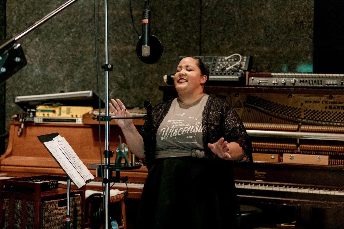 Emily Ware singing at a studio microphone with hands raised