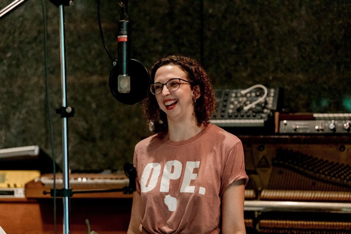 Taylor Goodine laughing at a studio vocal microphone in an Ope T-shirt