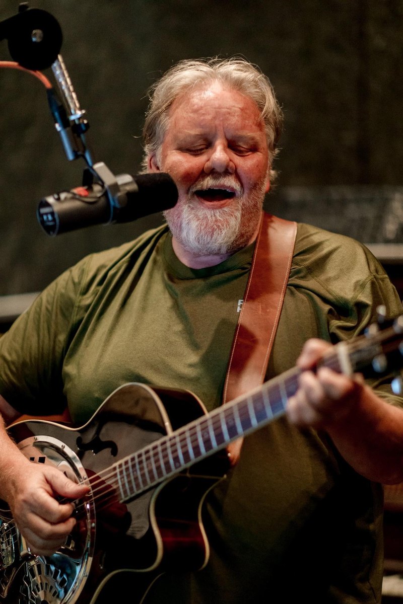 Mike Caucutt singing into a microphone while playing a resonator guitar