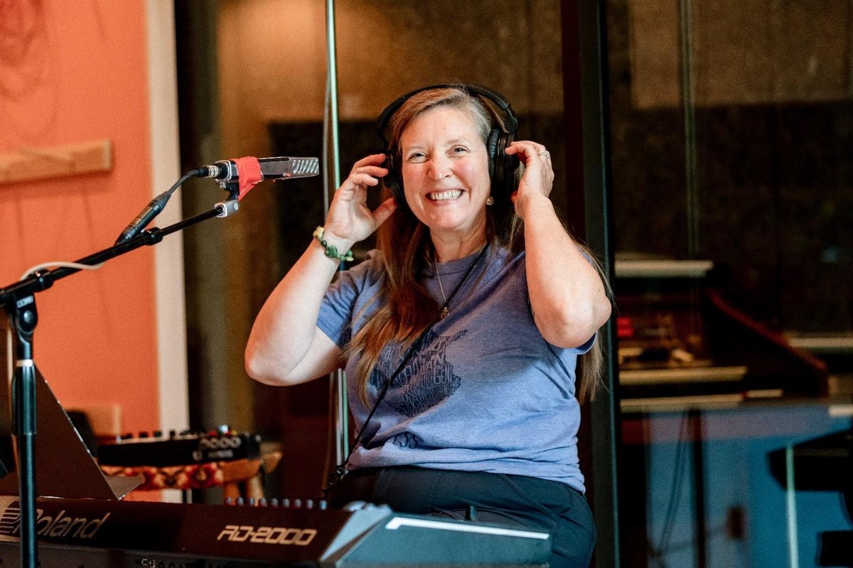 Nancy Caucutt smiling at her keyboard in the studio with headphones on